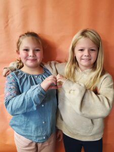 two students making a heart shape with their hands 